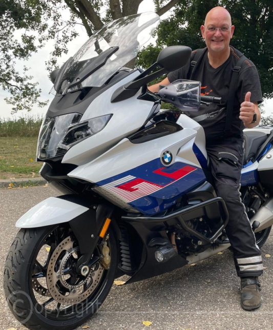 Foto van motorinstructeur in motorkleding naast motor